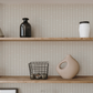 Stylized shelf in neutral tones with modern understated striped wallpaper that has random scattered floral motifs.