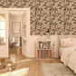 Children's room with pink and green floral berry wallpaper, dollhouse, and toys on a wooden floor.