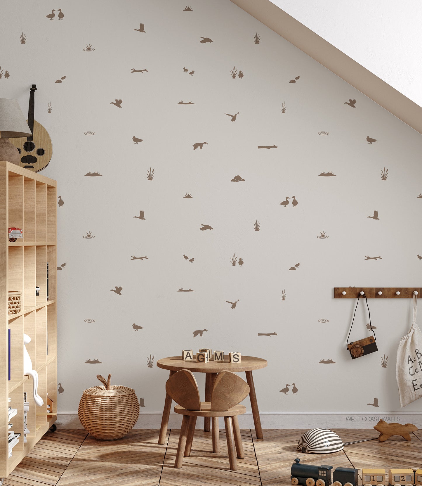 A neutral styled children's playroom corner with a white wall covered in small soft brown duck pond theme decals, a wooden shelf, a small round table and chair, a woven basket, and a toy train on the floor.