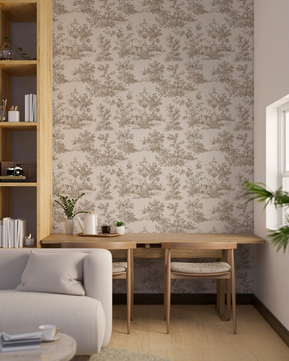 A styled interior room showing a wall covered in a beige and taupe toile-style floral wallpaper, with a wooden desk and chair, a light gray sofa, and a tall open shelving unit.