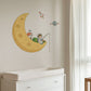 A wall decal featuring a cartoon astronaut fishing from a crescent moon with a small rocket and planet, shown applied to a beige wall above a white dresser in a nursery setting.