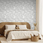 Modern bedroom with a brown upholstered bed and decorative pillows against a modern floral knockout style wallpaper in a warm grey and white