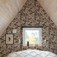 Small a-frame bedroom with floral blackberry and raspberry wallpaper, a window, and a bed.