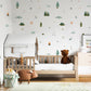 A styled children's bedroom featuring a light wood single bed with a white house-shaped canopy, a brown teddy bear, and a white dresser. The wall is decorated with whimsical, multi-colored forest-themed decals, and a framed sign on the right reads 'BORN TO BE WILD'.