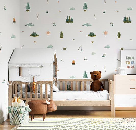 A styled children's bedroom featuring a light wood single bed with a white house-shaped canopy, a brown teddy bear, and a white dresser. The wall is decorated with whimsical, multi-colored forest-themed decals, and a framed sign on the right reads 'BORN TO BE WILD'.