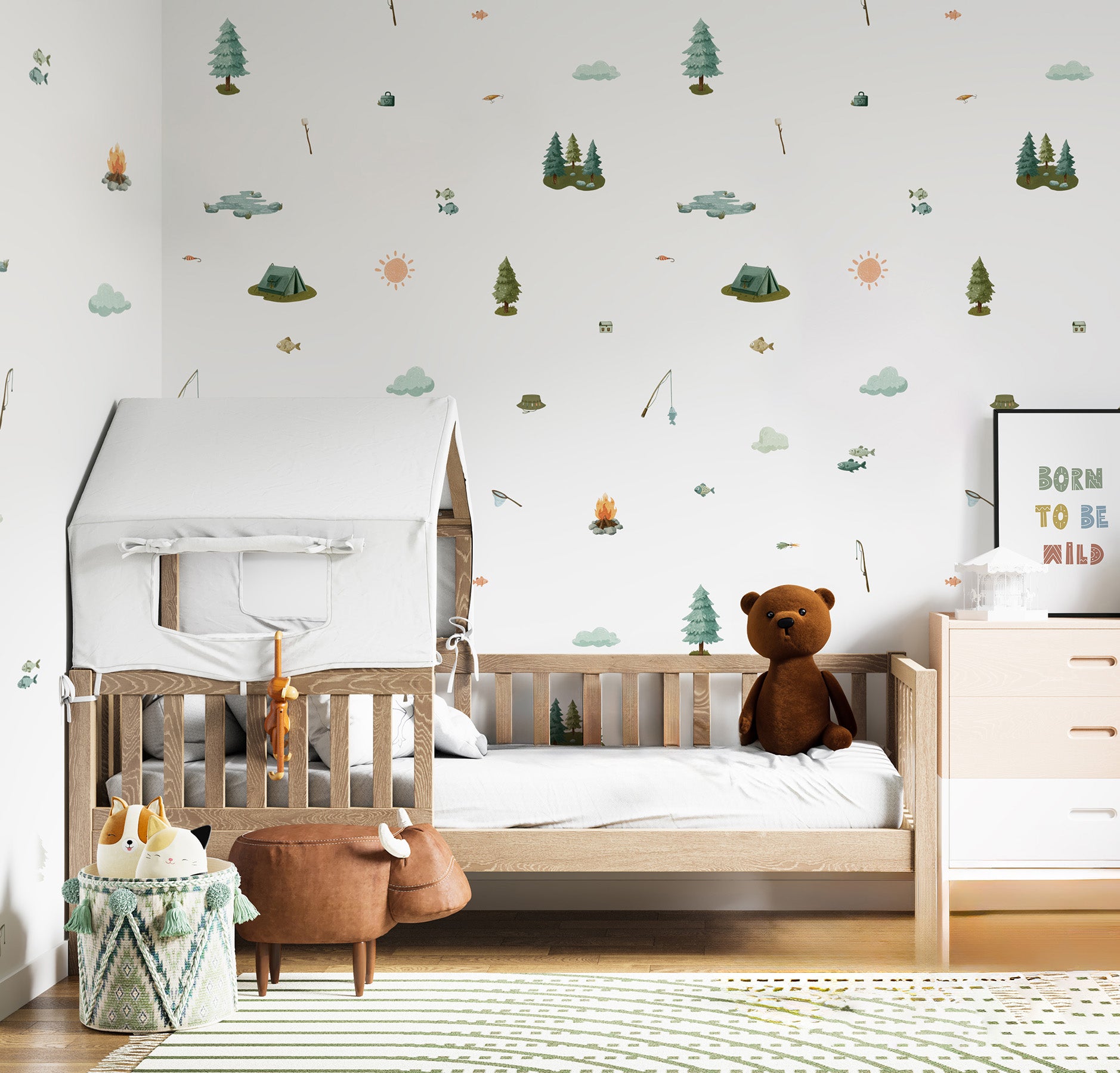 A styled children's bedroom featuring a light wood single bed with a white house-shaped canopy, a brown teddy bear, and a white dresser. The wall is decorated with whimsical, multi-colored forest-themed decals, and a framed sign on the right reads 'BORN TO BE WILD'.