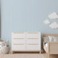 Children's bedroom with white dresser, wooden bed, and decorative clouds on a soft light blue faintly striped wallpaper.