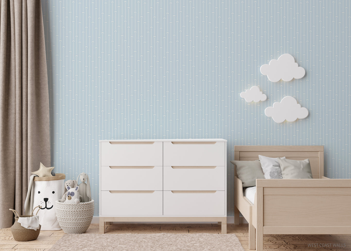 Children's bedroom with white dresser, wooden bed, and decorative clouds on a soft light blue faintly striped wallpaper.