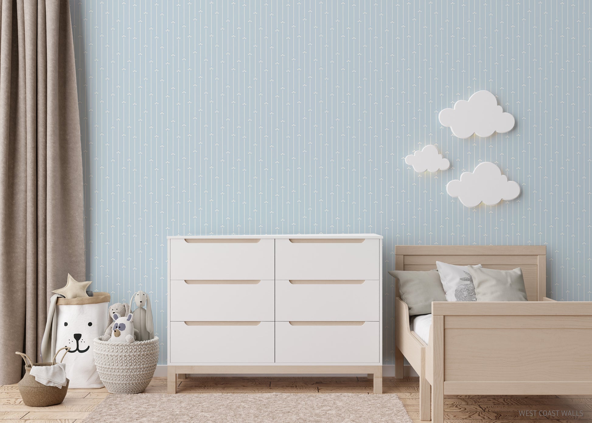 Children's bedroom with white dresser, wooden bed, and decorative clouds on a soft light blue faintly striped wallpaper.