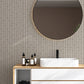 Modern bathroom vanity with round mirror and simple pinstripe beige and dark brown wallpaper with floral accents. 