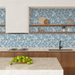 Modern kitchen with wooden cabinets, a floral knockout style wallpaper in a dusky blue and white, and a bowl of apples on the counter.