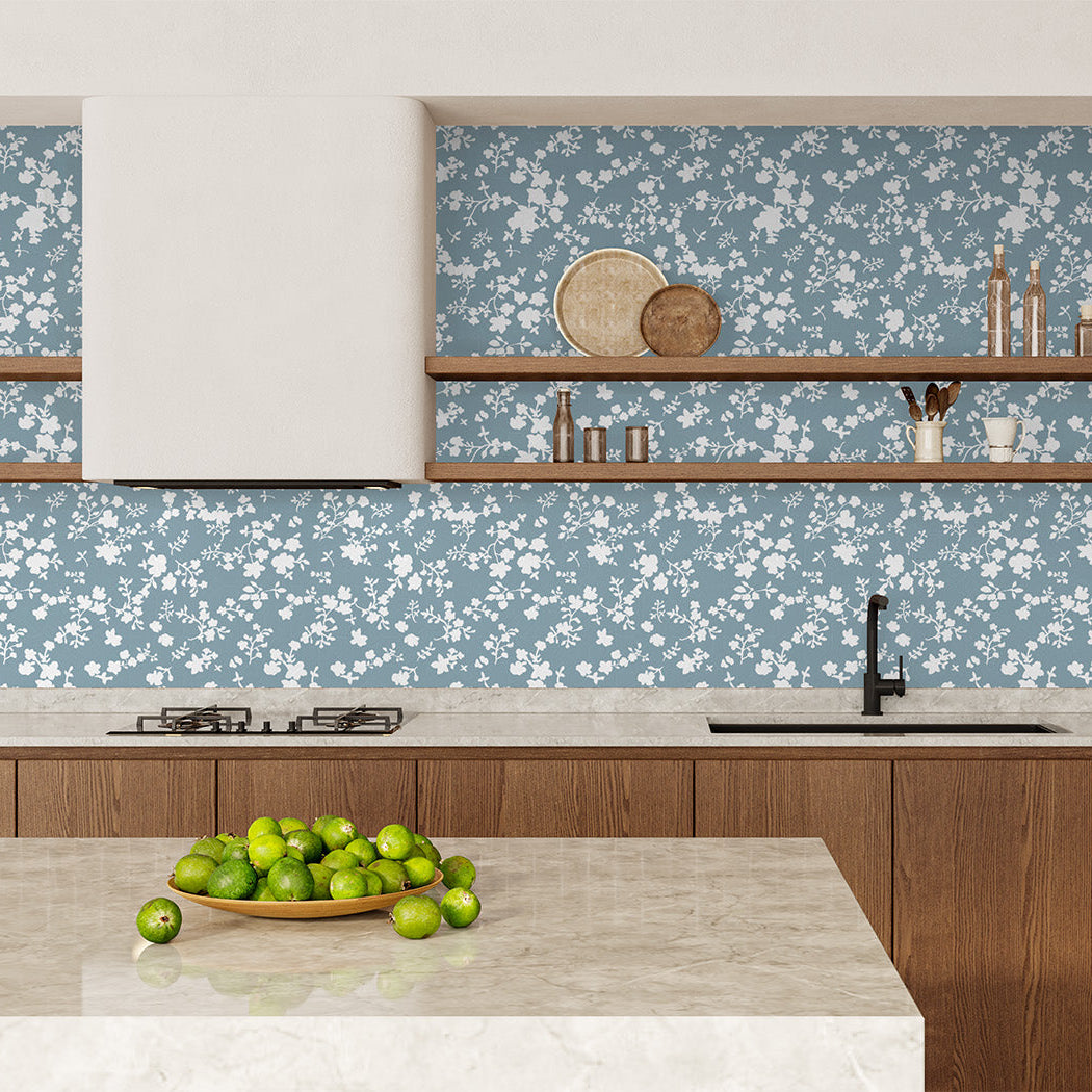 Modern kitchen with wooden cabinets, a floral knockout style wallpaper in a dusky blue and white, and a bowl of apples on the counter.