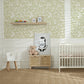 Nursery room with crib, teddy bear, and decorative items against a light green knockout style floral wallpaper wall, framed within the wall moulding.