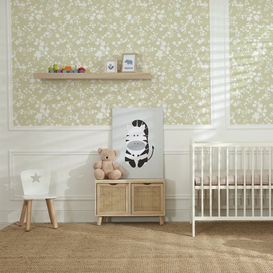 Nursery room with crib, teddy bear, and decorative items against a light green knockout style floral wallpaper wall, framed within the wall moulding.