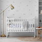 A styled nursery interior featuring subtle grey duck pond themed wall decals behind a white wooden crib with white bedding. 