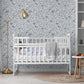 Nursery room with a white crib, blue forest  and floral theme wallpaper, and neutral wooden floor. 