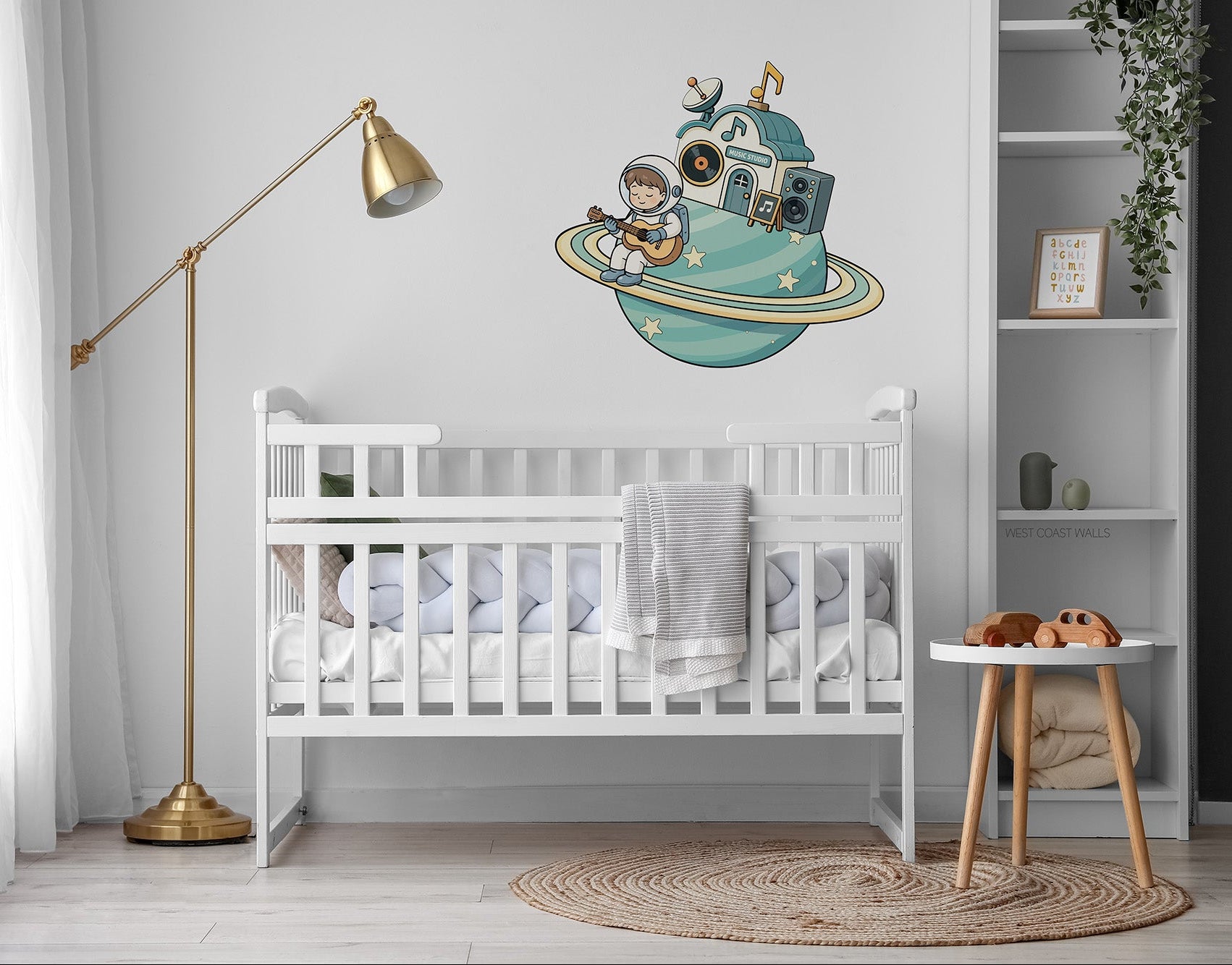A wall decal of a cartoon astronaut sitting on a teal-blue music themed planet while playing guitar. It is displayed on a white wall above a white wooden baby crib in a styled nursery room.