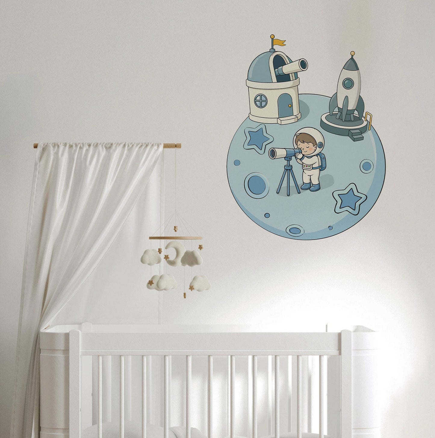 A nursery wall decal featuring a cartoon astronaut, space station, and rocket on a blue moon, shown above a white crib with a white canopy and cloud mobile.