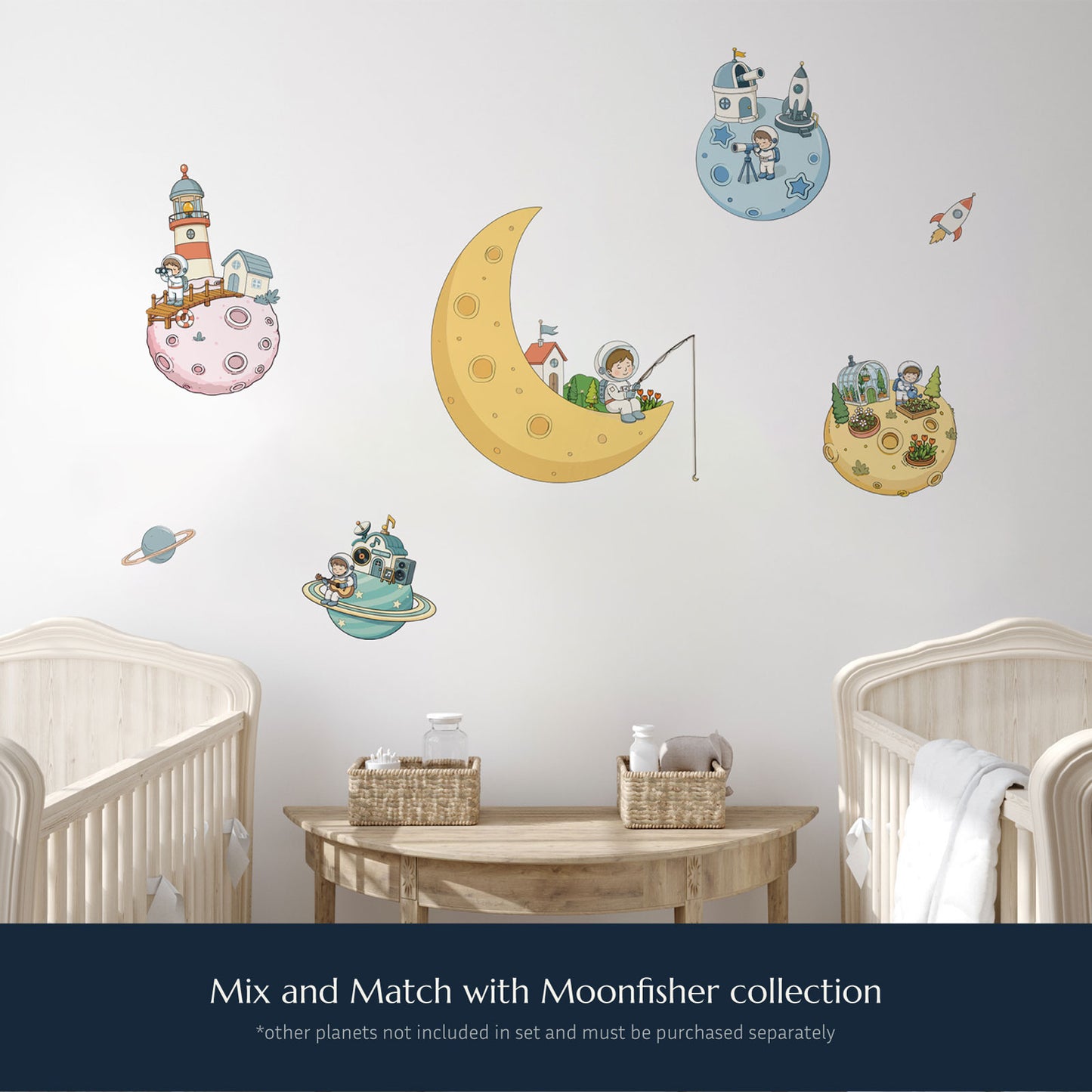 A set of whimsical space-themed wall decals displayed on a light gray wall above a wooden table and two cribs. The decals include a large yellow crescent moon with an astronaut fishing, several small planets with houses, a rocket ship, and a satellite, with text at the bottom reading 'Mix and Match with Moonfisher collection'. Additional planet decals are not included in the moonfisher set