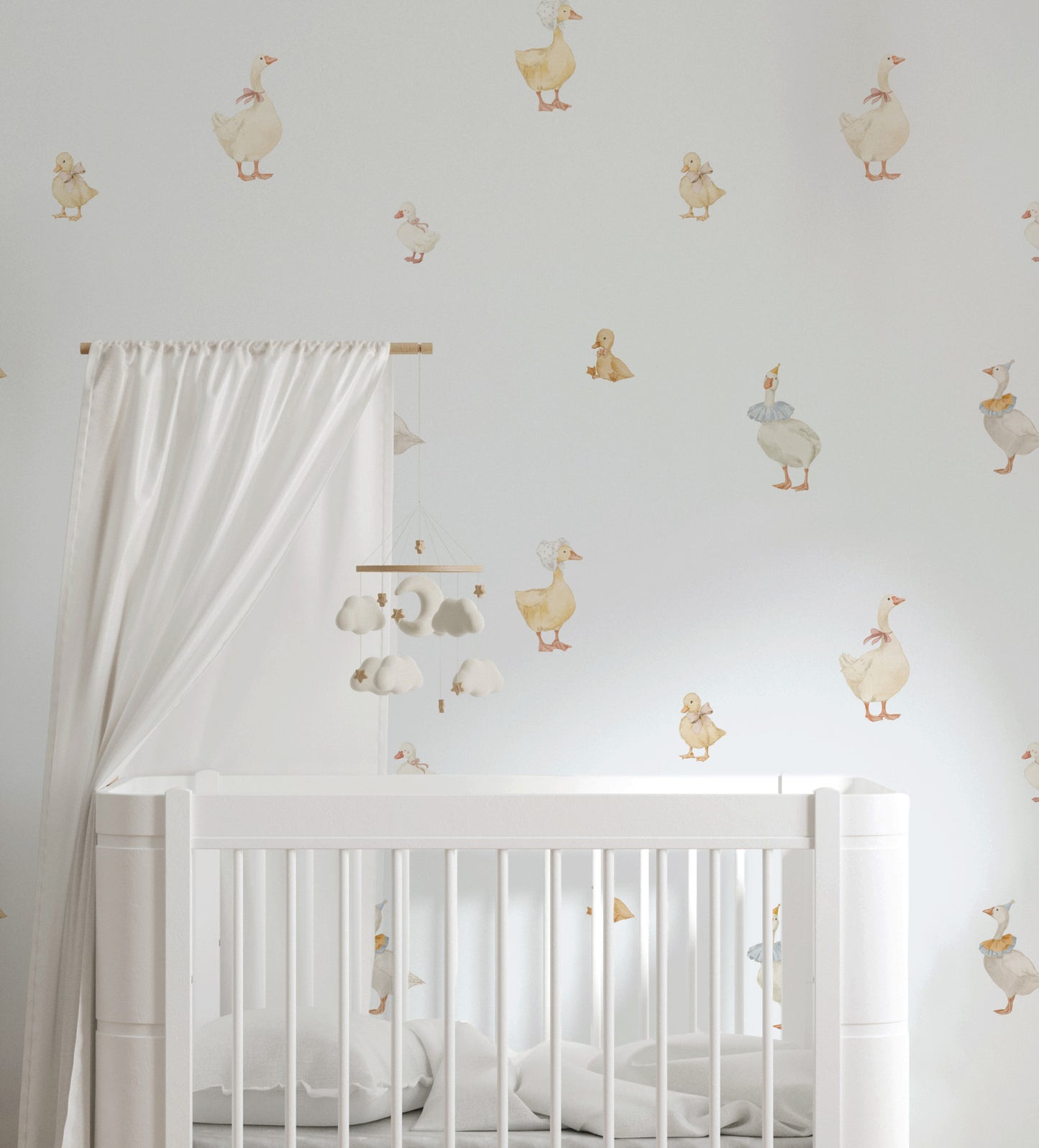 A white wooden baby crib in a nursery setting, decorated with whimsical duck and goose wall decals on a light gray wall. A white canopy curtain hangs from a wooden rod on the left, and a matching mobile hangs above the crib.