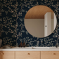 Modern bathroom with round mirror on floral branch wallpaper with navy background