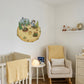 A styled nursery room featuring a whimsical cartoon planet wall decal with a child gardening, displayed on a white wall above a white wooden crib. The room also includes a cream armchair with a yellow blanket, a matching cream dresser, and a small shelf with decorative items.
